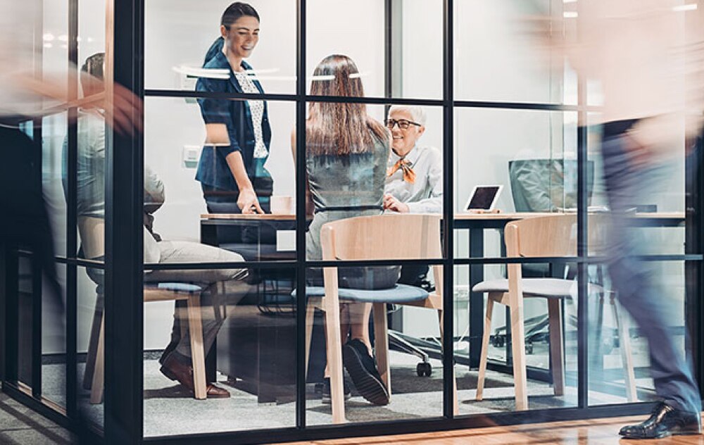 Image of a group of people in a glass conference room setting with people walking by